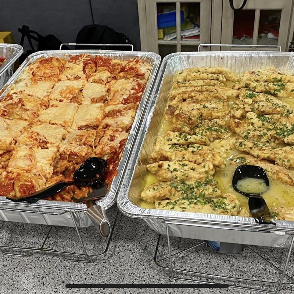 Trays of food on a table in front of a group of people.