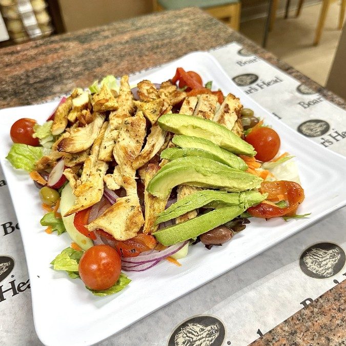 A chicken salad on a white plate with avocado and tomatoes.